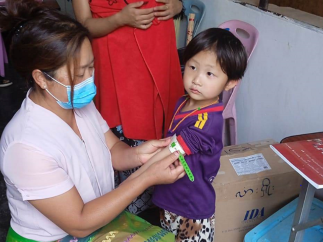 At the clinic of the internally displaced people camp, a health worker uses the mid-upper arm circumference measure (MUAC) to quickly identify if the child is at risk of malnutrition. When measured properly against a bare upper arm, the paper gauge provides a number and indicates the colour range. The green colour here is positive - the child is not showing signs of malnutrition.